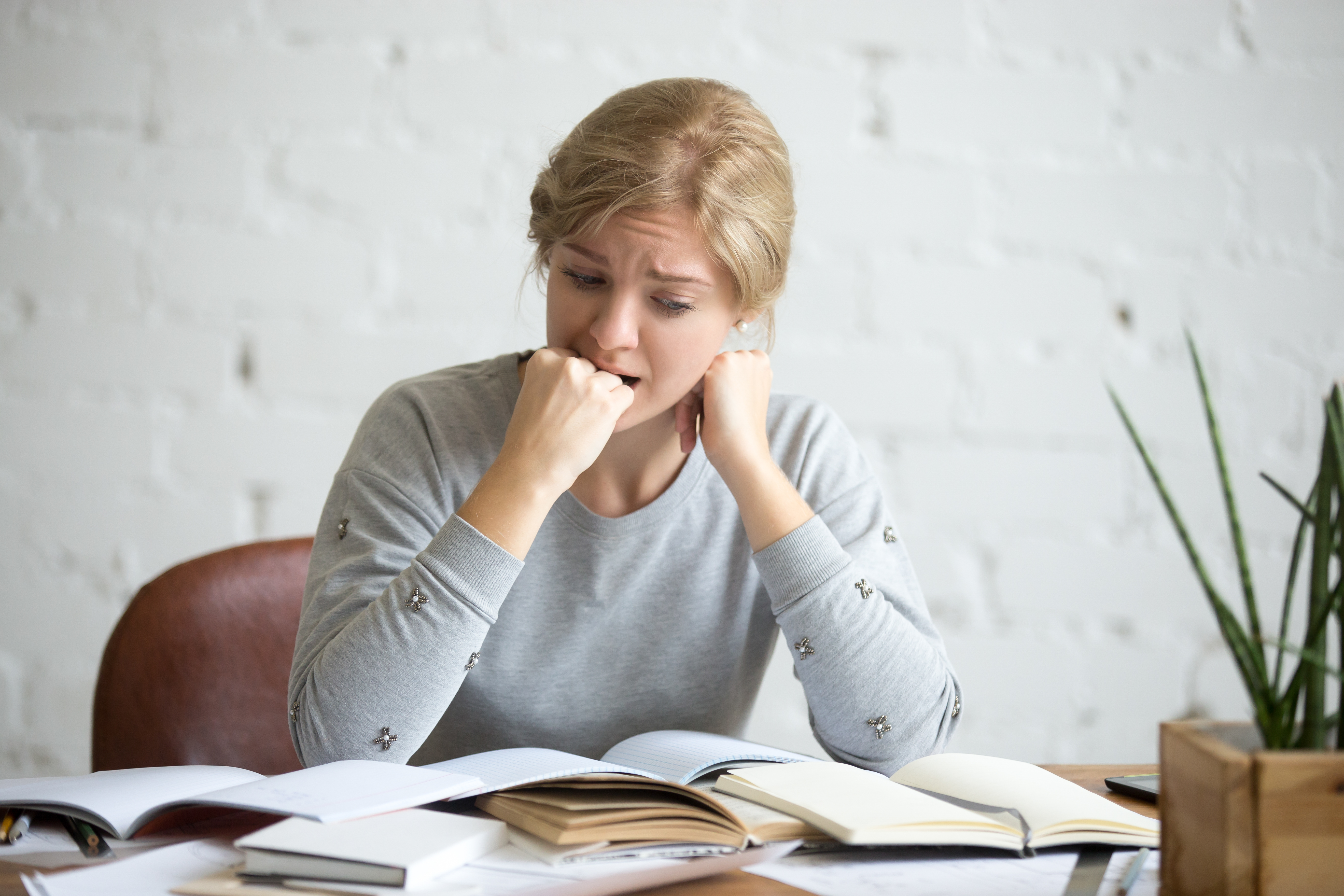 portrait of a student girl sitting at the desk biting her fist