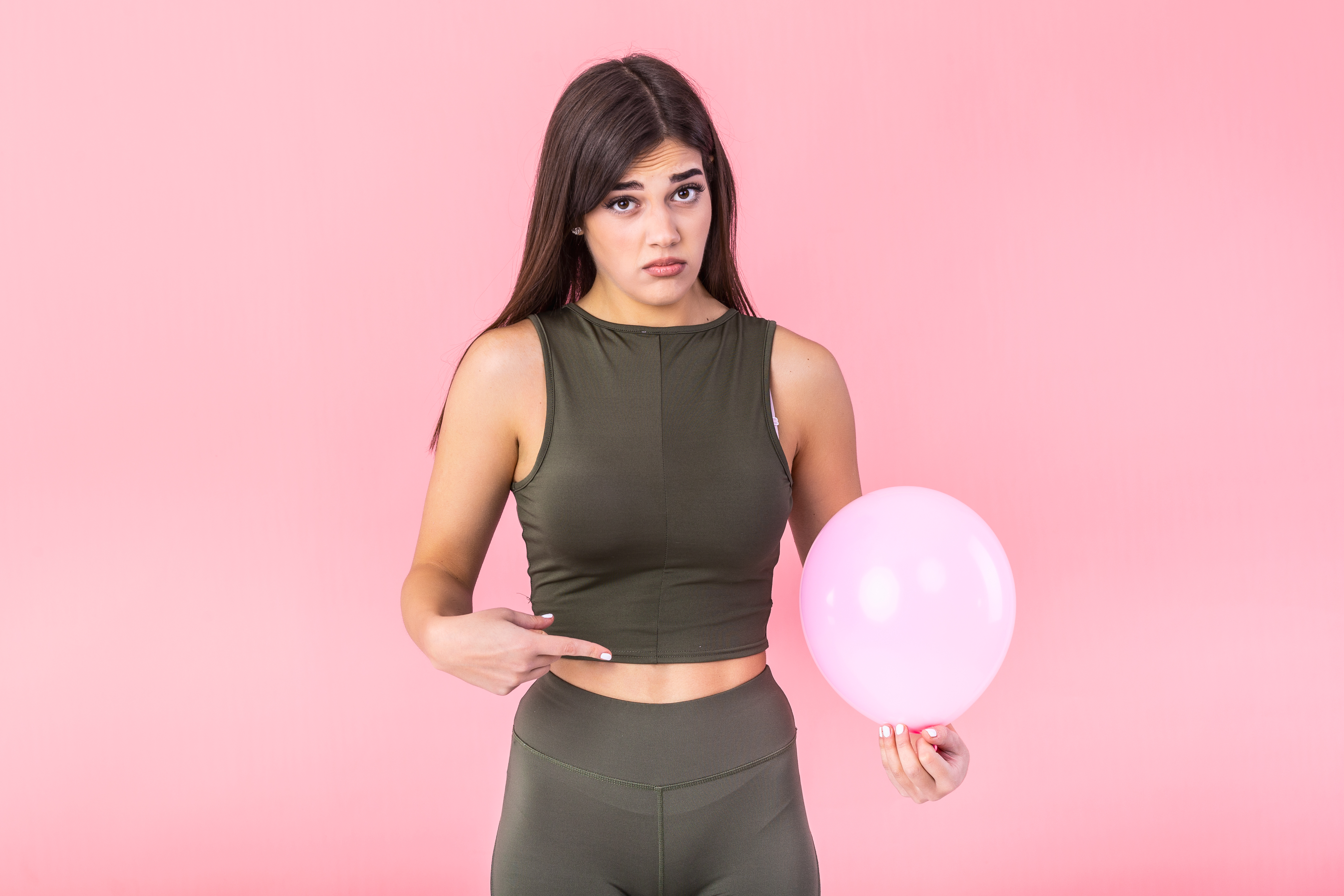 beautiful young woman holding pink balloon feeling bloated